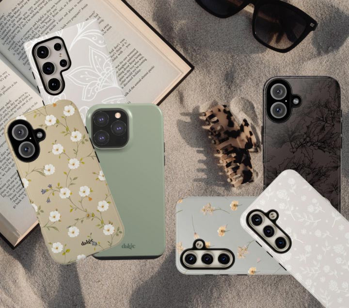 Six floral and nature-inspired phone cases are displayed on a textured surface, alongside an open book, black sunglasses, and a small animal print claw hair clip.