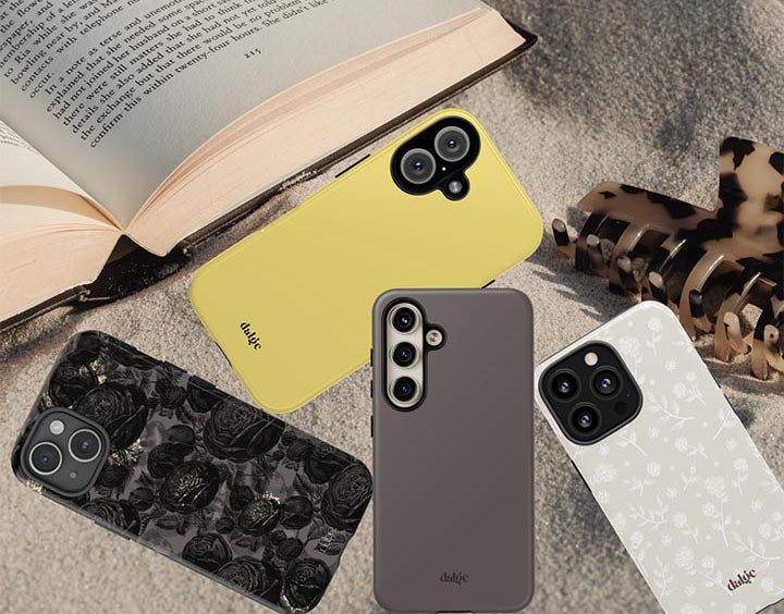 Four floral and solid color phone cases are displayed with an open book and a small animal print claw clip on a textured surface.