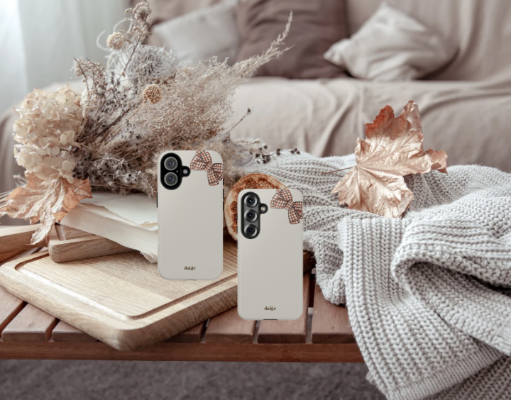 Two smartphones with white cases featuring brown bow designs on a wooden surface with decorative elements.