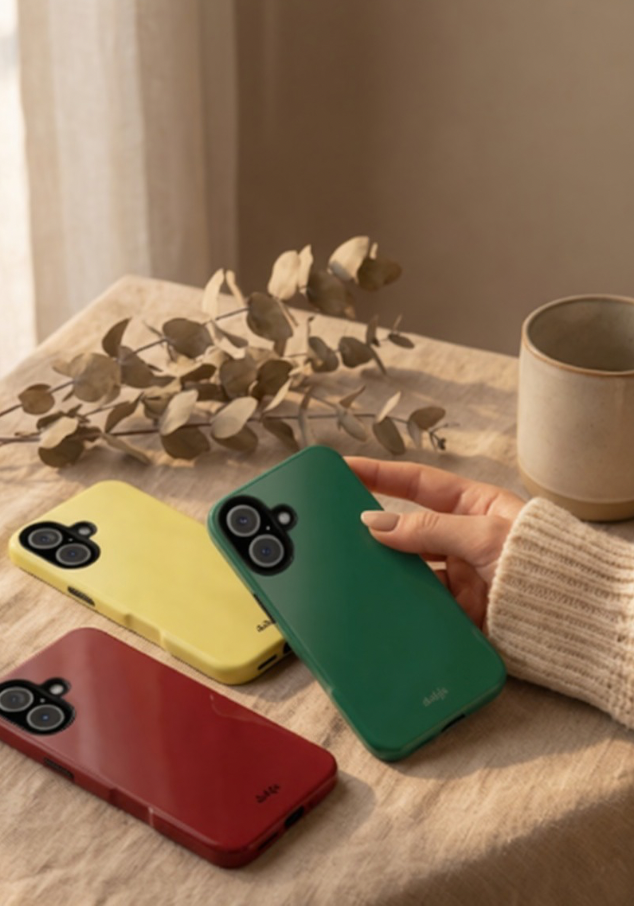 Solid color phone cases in green, yellow, and red on a wooden table with a hand holding the green case from our collection My Solids with glossy solid color phone cases.