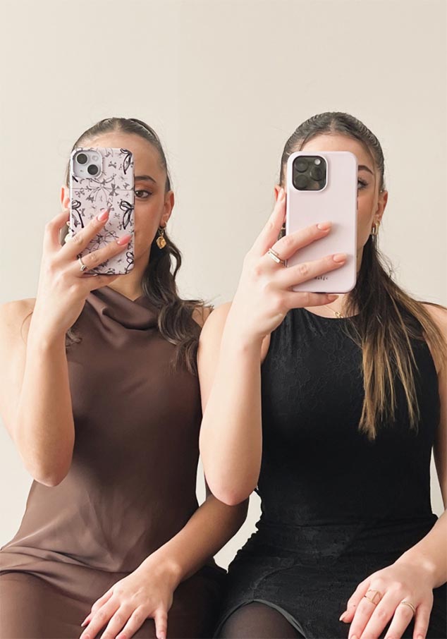 Two women seated, showcasing iPhone cases—one with a black and white abstract design, the other in solid pink