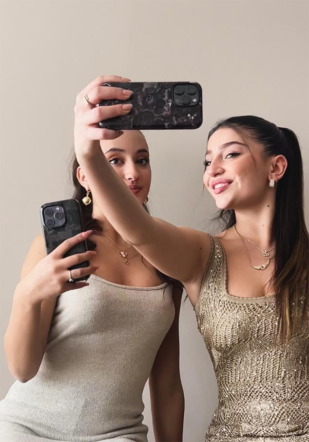 Two women in beige dresses taking a selfie, holding iPhones with dark academia floral designs and the "Dalge" logo at the bottom.