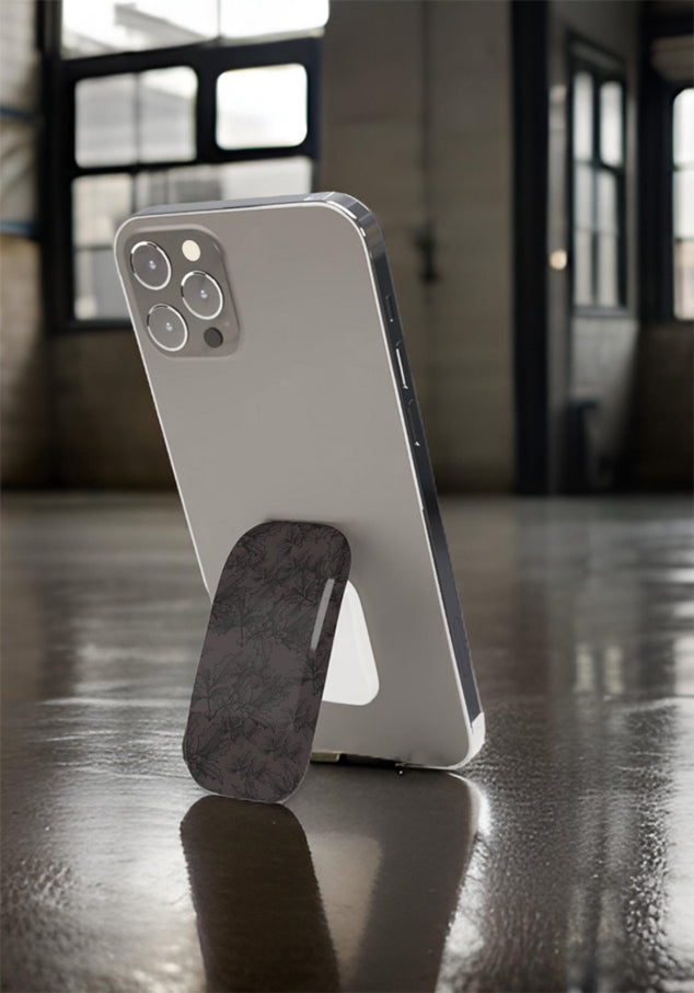 Close up of an iphone standing using a dark floral glossy finish Phone grip on a glolssy grey floor with industrial windows 