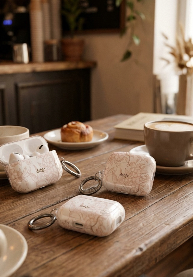 Pastel Floral wireless earbuds case on a wooden table with coffee and pastries.